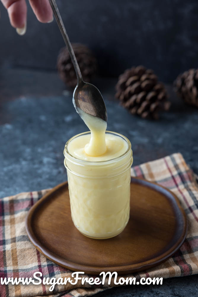 glass jar of condensed milk on a plate with a spoon dipping in