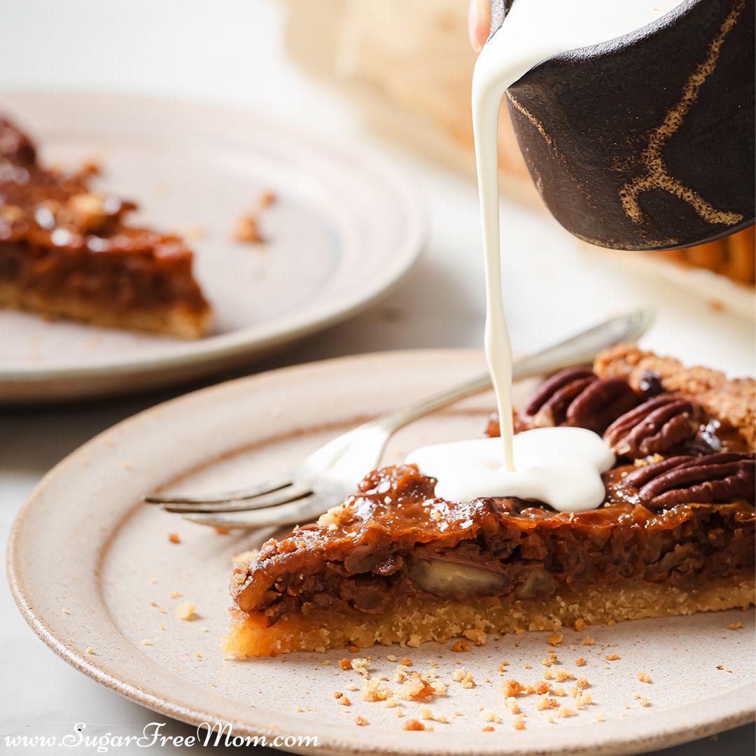 slice of pecan pie on a plate getting cream sauce poured over the top