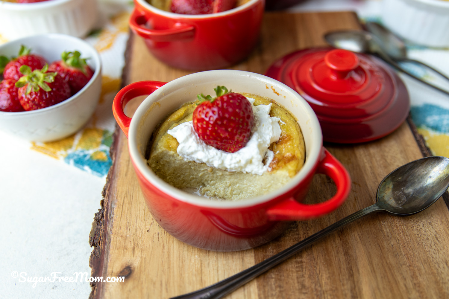 Sugar free low carb keto coconut custard baked in red ramekins topped with fresh strawberries.