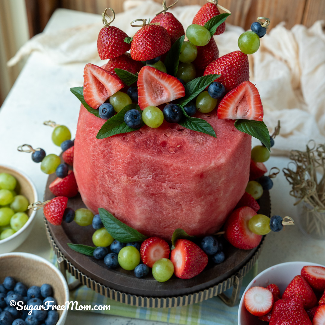 close up pic of a fresh fruit watermelon cake on a stand with fruit skewers