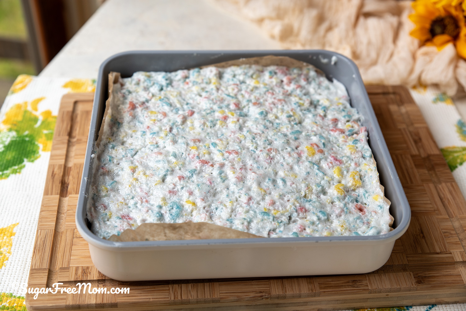 horizontal image of keto marshmallow rice krispie treats in a 9 by 9 pan on cutting board