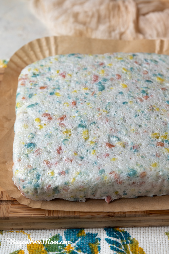 vertical image of keto marshmallow rice krispie treats removed from 9 by 9 pan sitting on parchment paper on cutting board