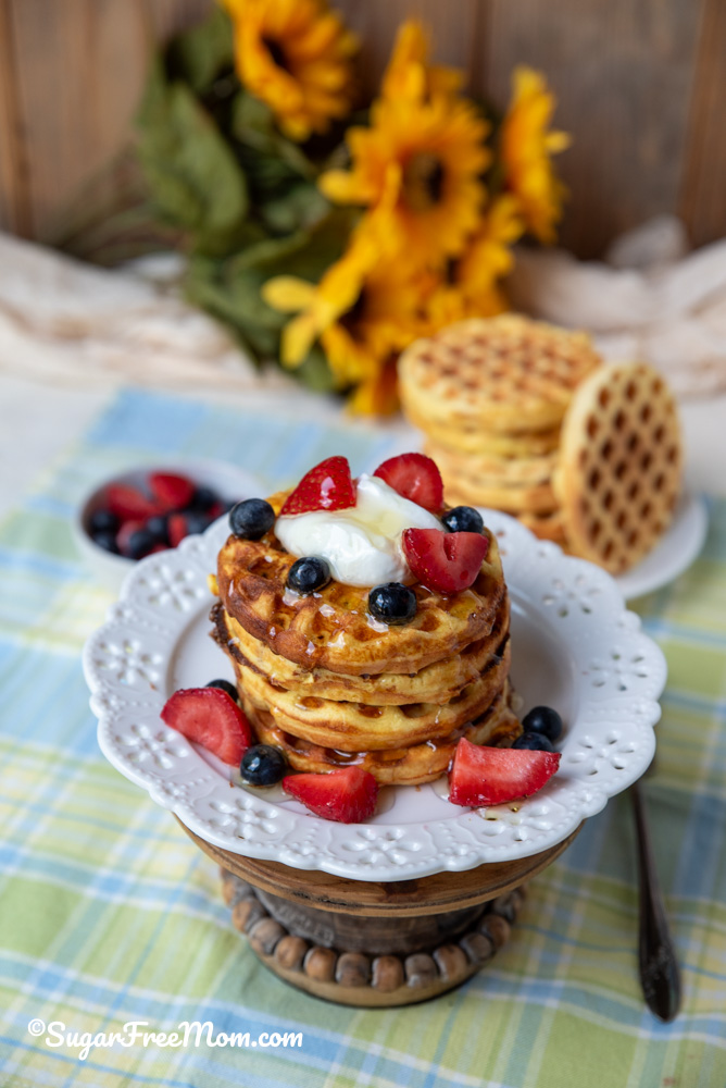 stacked keto coconut flour waffles topped with berries on a white plate and cake stand