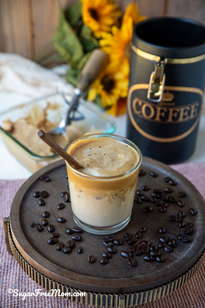 melted keto frozen whipped Dalgona coffee in a glass with a wooden spoon sitting on a tray with coffee beans