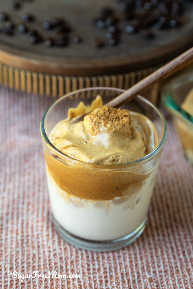 vertical image of a glass of Dalgona frozen whipped coffee in a glass with wooden spoon