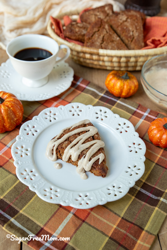 keto pumpkin ricotta scone with maple cream cheese glaze sitting on a white plate with coffee in the background