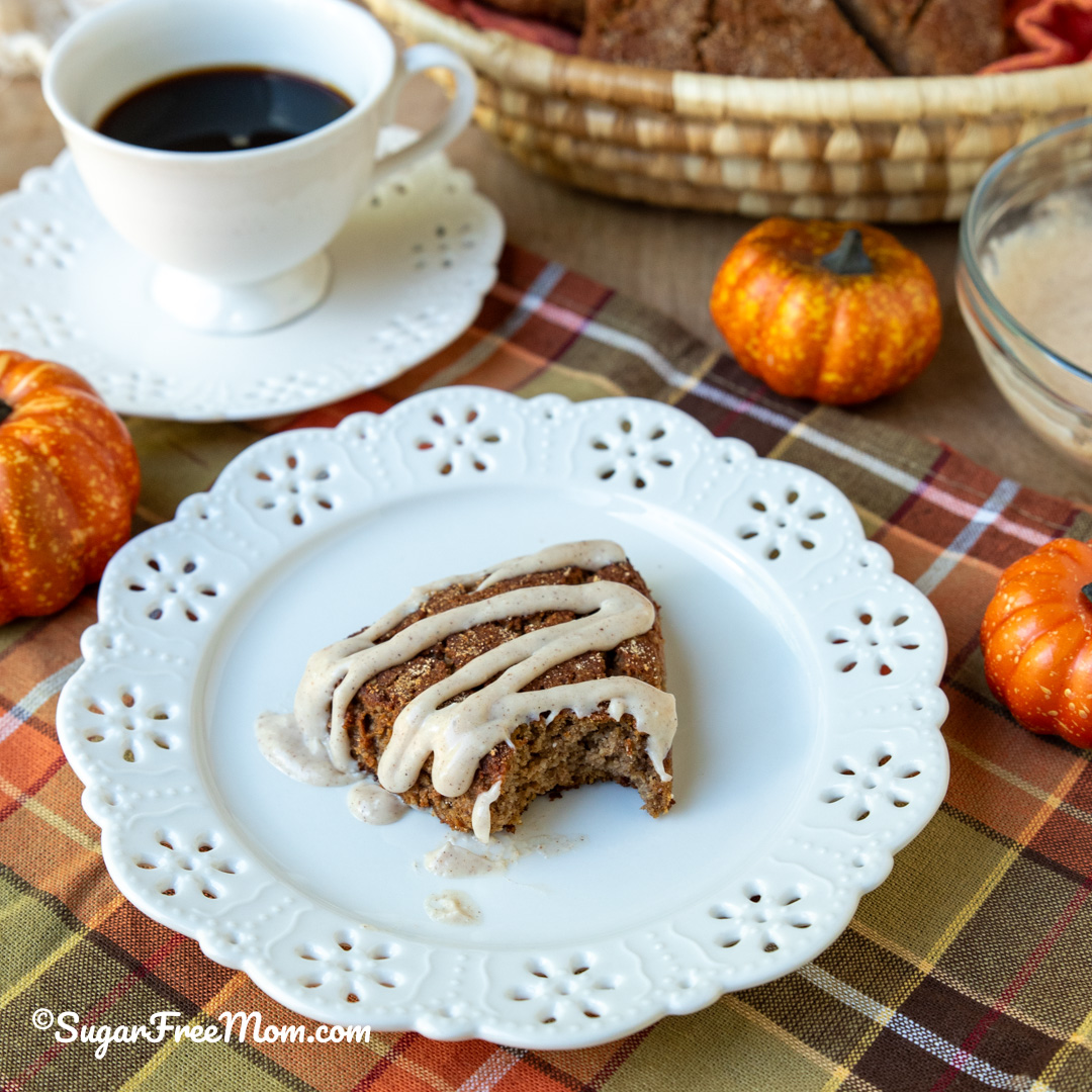 square image of keto pumpkin scone on a plate with pumpkins in background and coffee