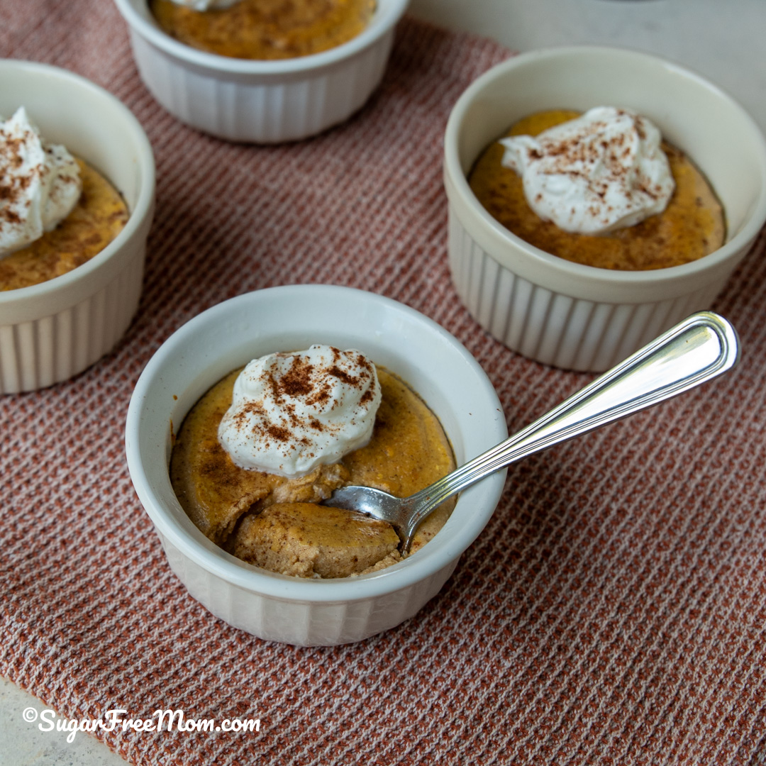 Square image of low carb pumpkin ricotta custard in small ramekin with a spoonful and topped with whipped cream