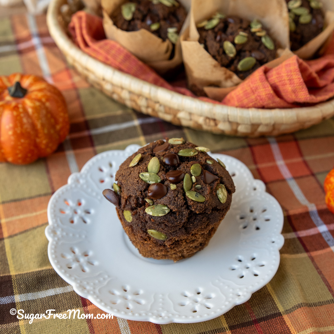 unwrapped chocolate pumpkin muffin on a white plate topped with pumpkin seeds and chocolate chips
